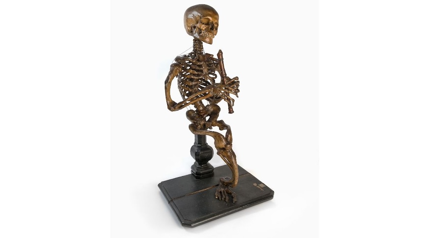 A seated skeleton with one leg holding a wooden recorder