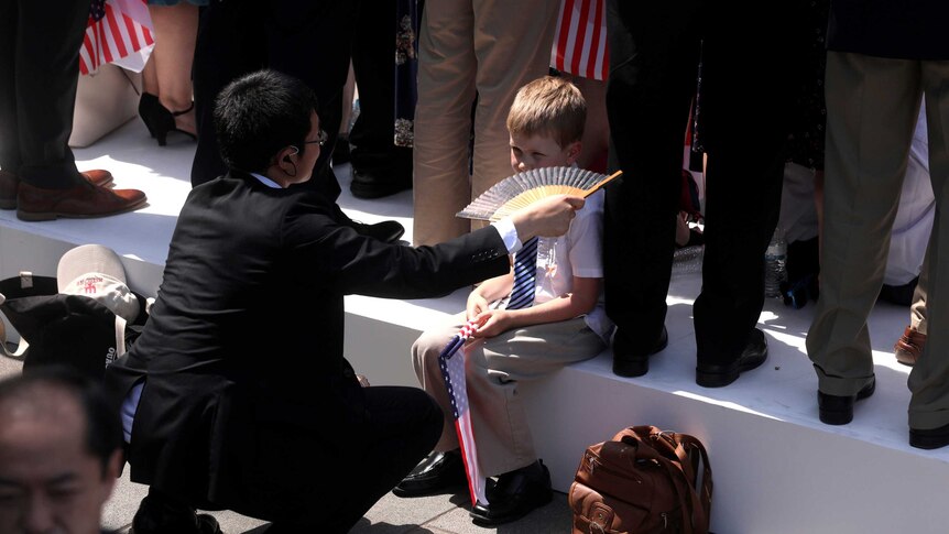 A man in a suit fans a young child holding a US flag.