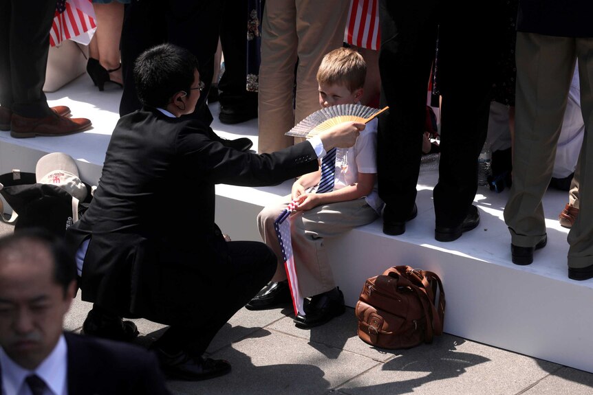 A man in a suit fans a young child holding a US flag.