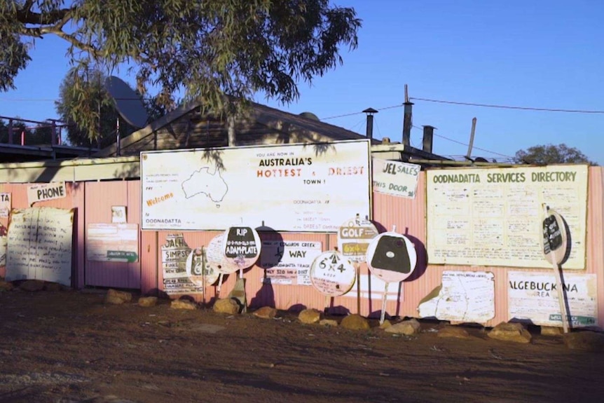 More than a dozen pink signs of varying sizes stand next to a pink wall with descriptions of travel advice for Oodnadatta.