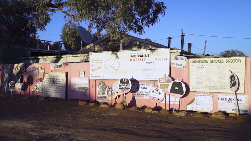 More than a dozen pink signs of varying sizes stand next to a pink wall with descriptions of travel advice for Oodnadatta.