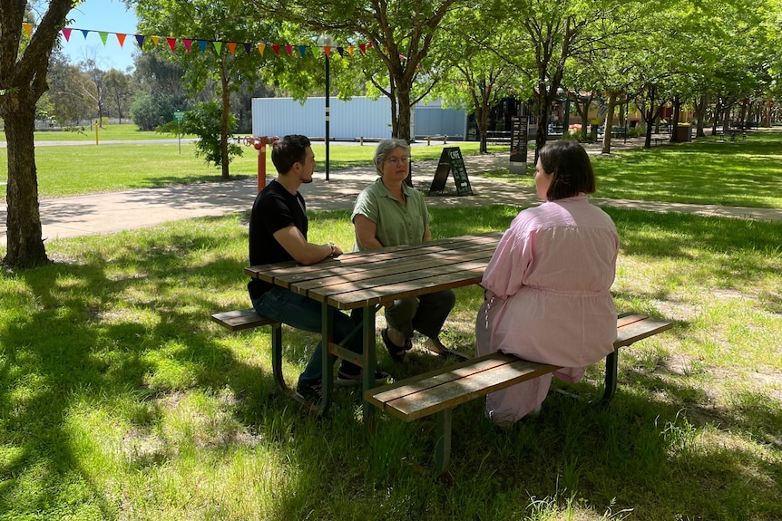Three people sitting at an outdoor table.