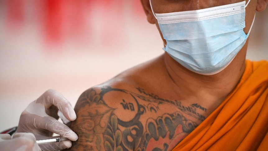 A monk dressed in traditional orange cloth gets a vaccine in his arm. 