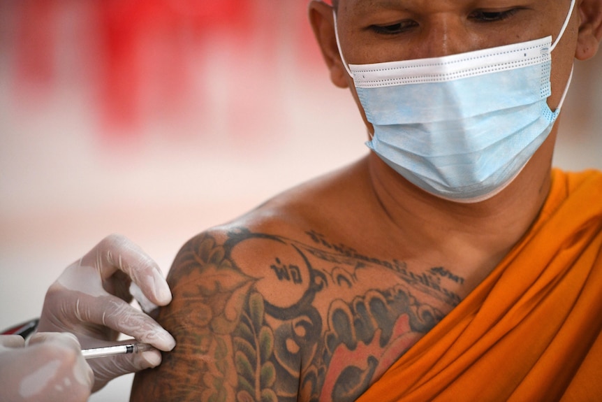 A monk dressed in traditional orange cloth gets a vaccine in his arm. 