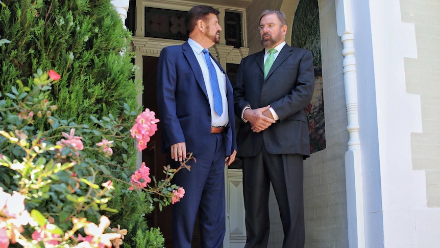 Tim Jeffery and Simon Turner stand outside a building, with shrubs in the foreground.