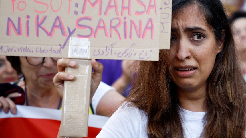 A distract woman holds a sign with the names of women who have been killed in Iran during a protest.