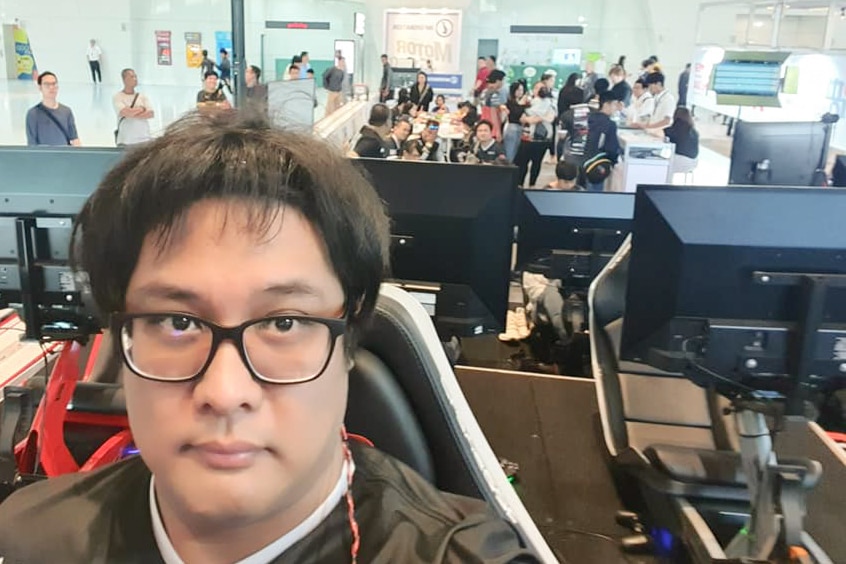 A man wearing glasses looks at computer screen while people work in the background behind him.