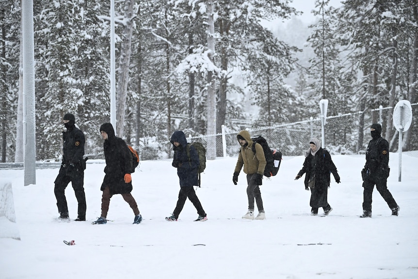 Two border guards escort a group of migrants carrying backpacks as they walk in the snow