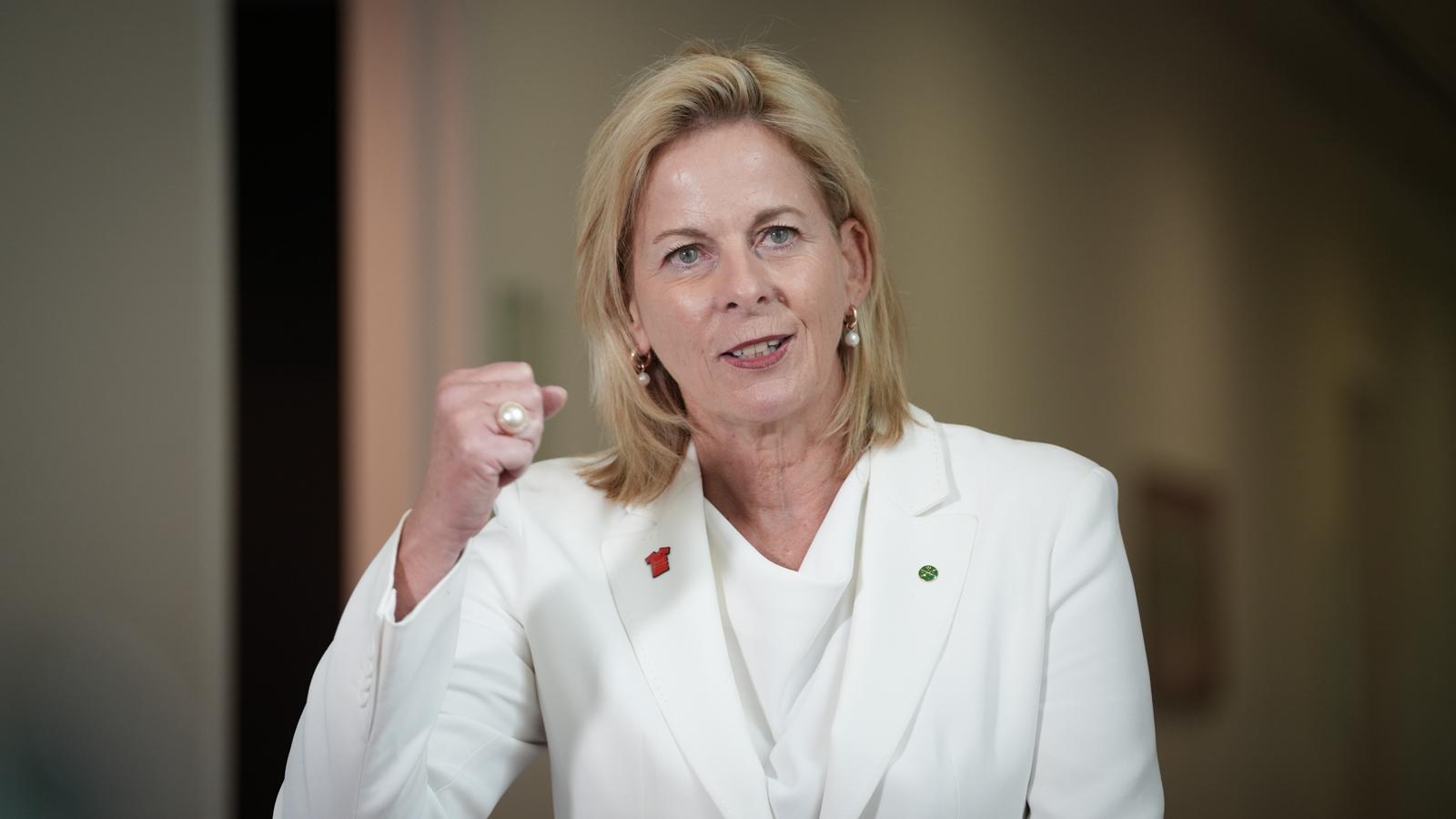 A woman wearing a white suit speaks while raising a fist.
