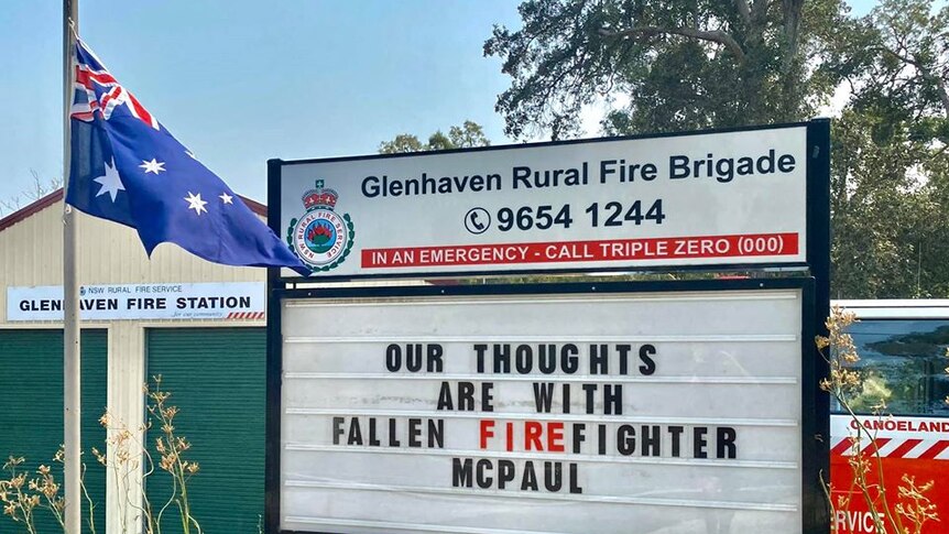 An Australian flag is flown at half mast with a message that reads: "our thoughts are with fallen firefighter McPaul".