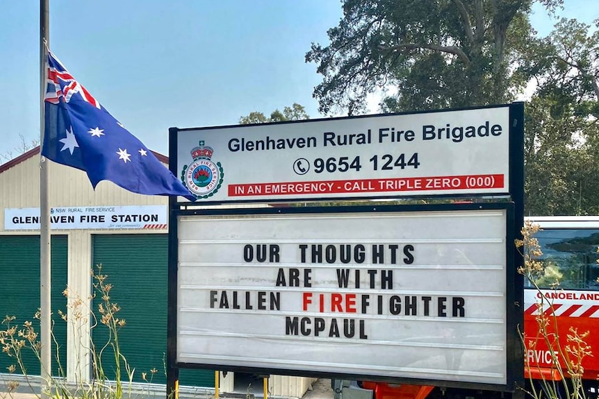 An Australian flag is flown at half mast with a message that reads: "our thoughts are with fallen firefighter McPaul".