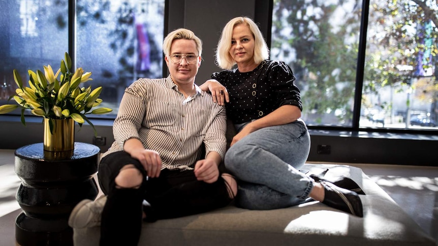 A man and a woman smile at the camera, sitting