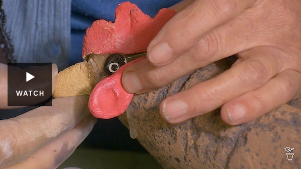 A beak being attached to a chicken ornament made from concrete. Has Video.