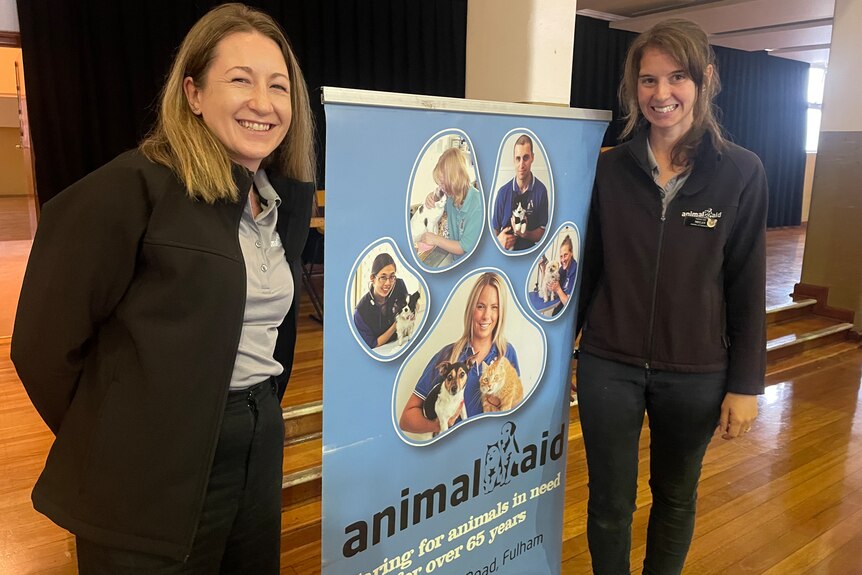 Two women standing on either side of an animal aid banner  