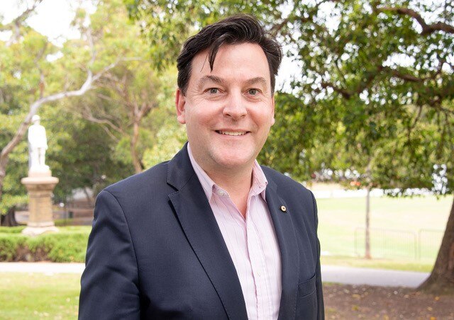 Professor Matthew Kiernan, wearing a light pink shirt and dark suit jacket stands in a park and looks at the camera