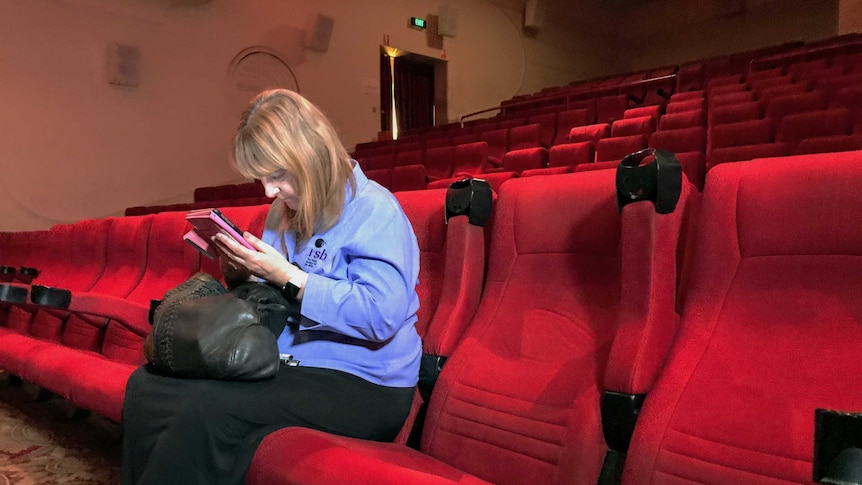A woman looks down at her smartphone screen while sitting in a near empty cinema.