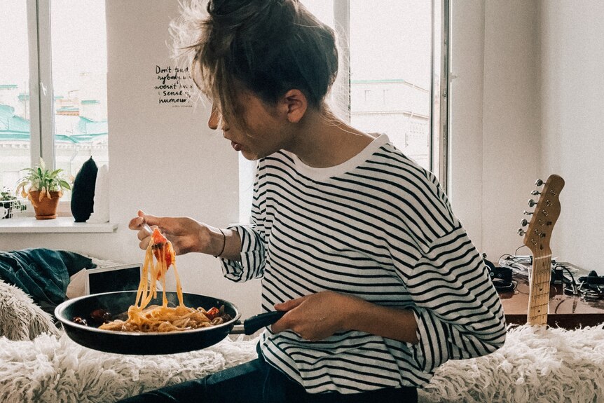 Person at home eating pasta from a saucepan, eating for comfort.