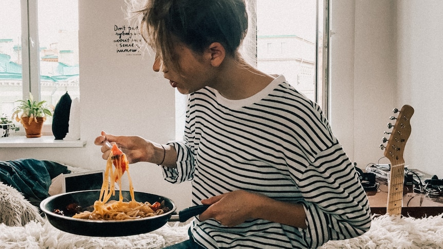 Person at home eating pasta from a saucepan, eating for comfort.