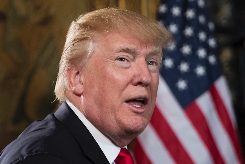 Tight shot of Donald Trump speaking with US flag behind him.