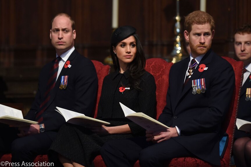 Megan Markle wears black attire and sits in between Prince Harry and Prince Williams.
