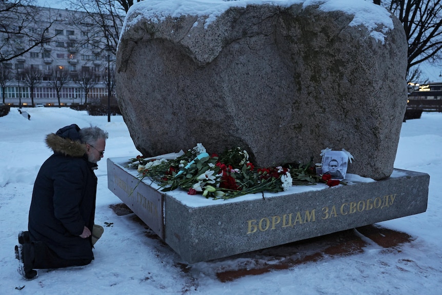 A man kneels at the monument to the victims of political repressions in St Petersburg following the death of Alexei Navalny.