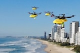 red and yellow drones flying above beach with high rise apartment buildings in the background.