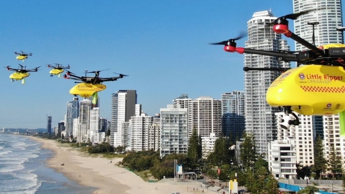 red and yellow drones flying above beach with high rise apartment buildings in the background.