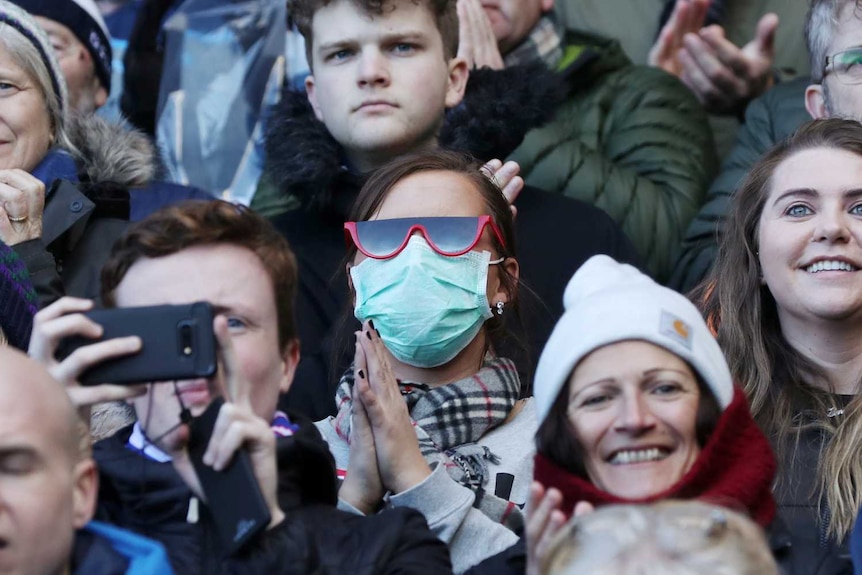 A fan inside a stadium wears a face mask while watching a rugby game