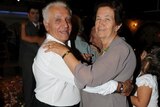 Irene and Peter Magriplis smile at the camera while dancing together at an event.