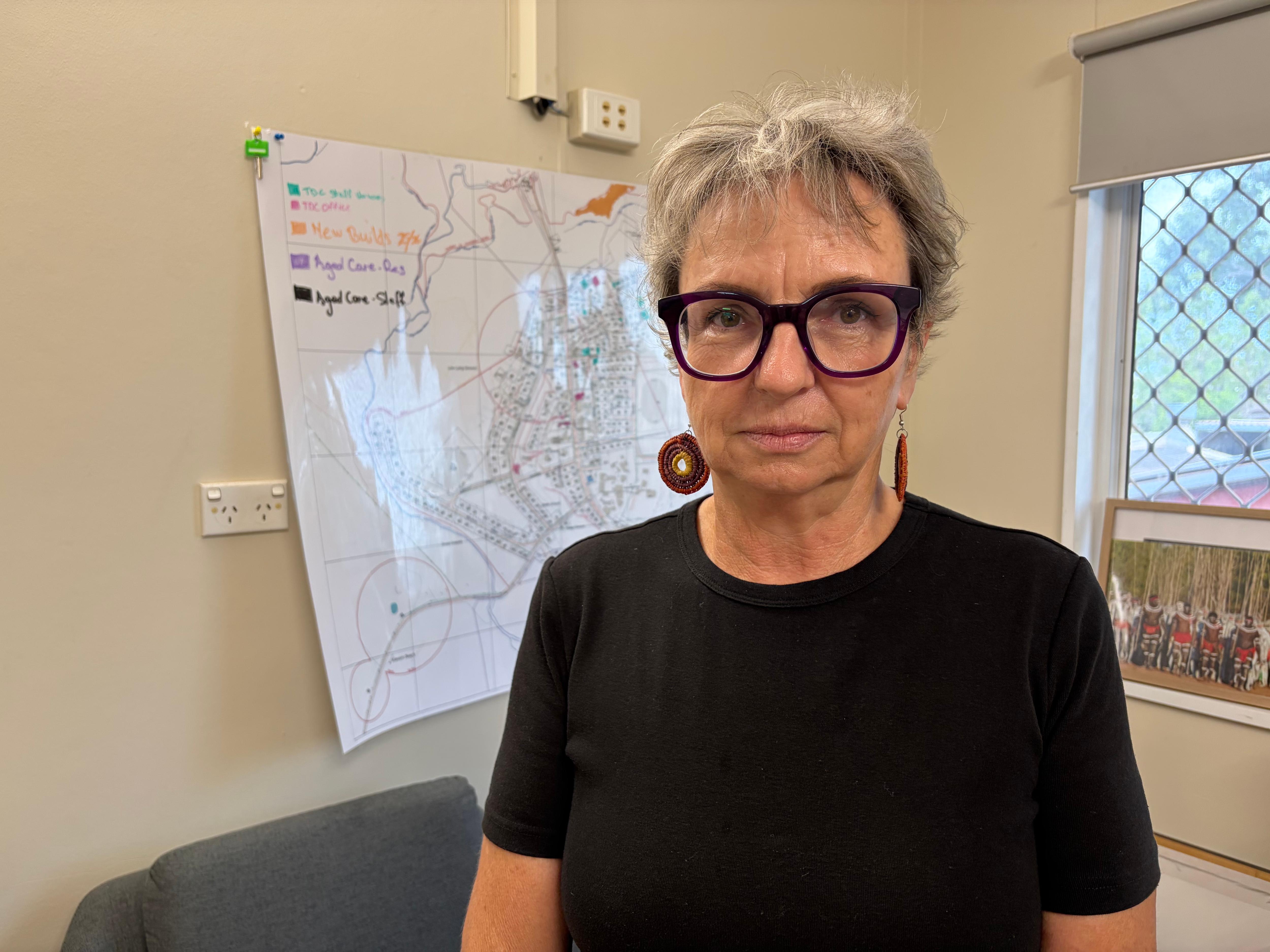 Tracey Leo stands in front of a white board wearing a black t-shirt and glasses.