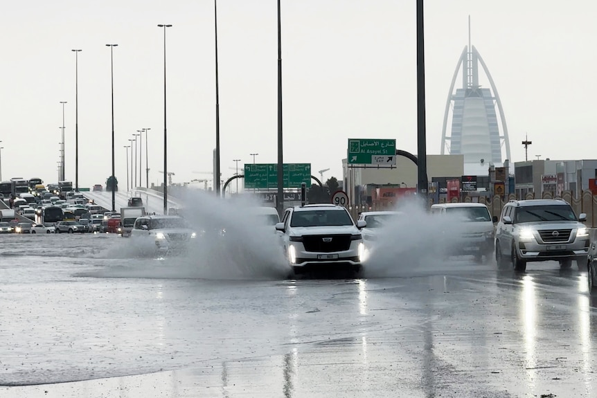 An SUV splashes through standing water on a road with the Burj Al Arab luxury hotel seen in the background in Dubai.