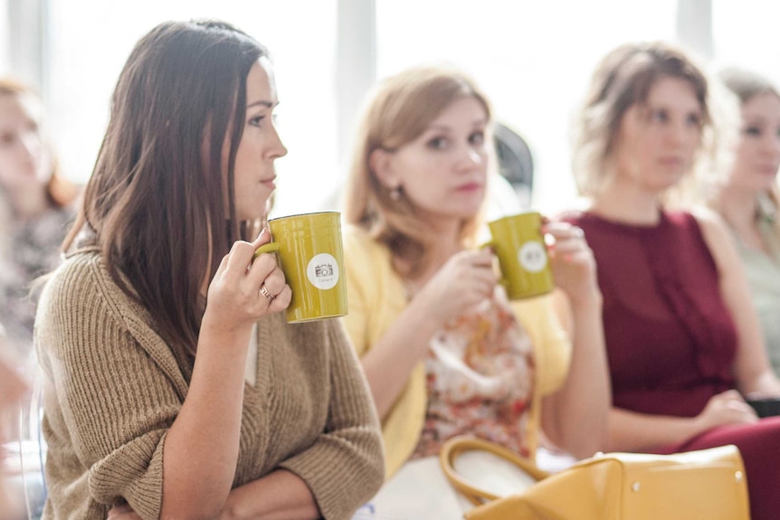 Three women sit in a row drinking from mugs
