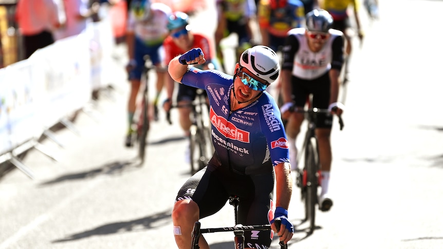 An Australian cyclist grimaces and punches the air in jubilation after winning a stage in a sprint.