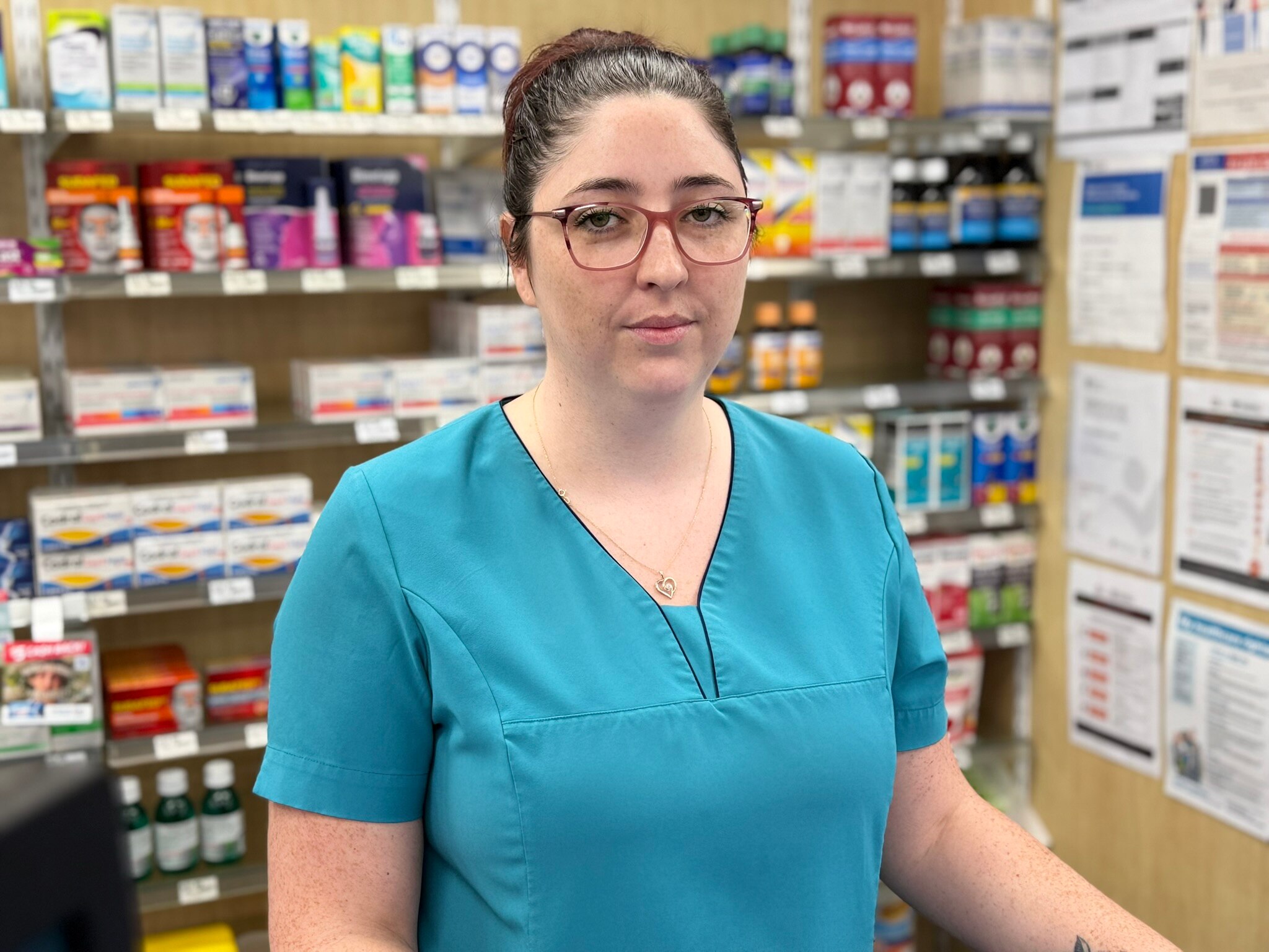 Uma mulher de cabelos escuros está atrás do balcão de uma farmácia.