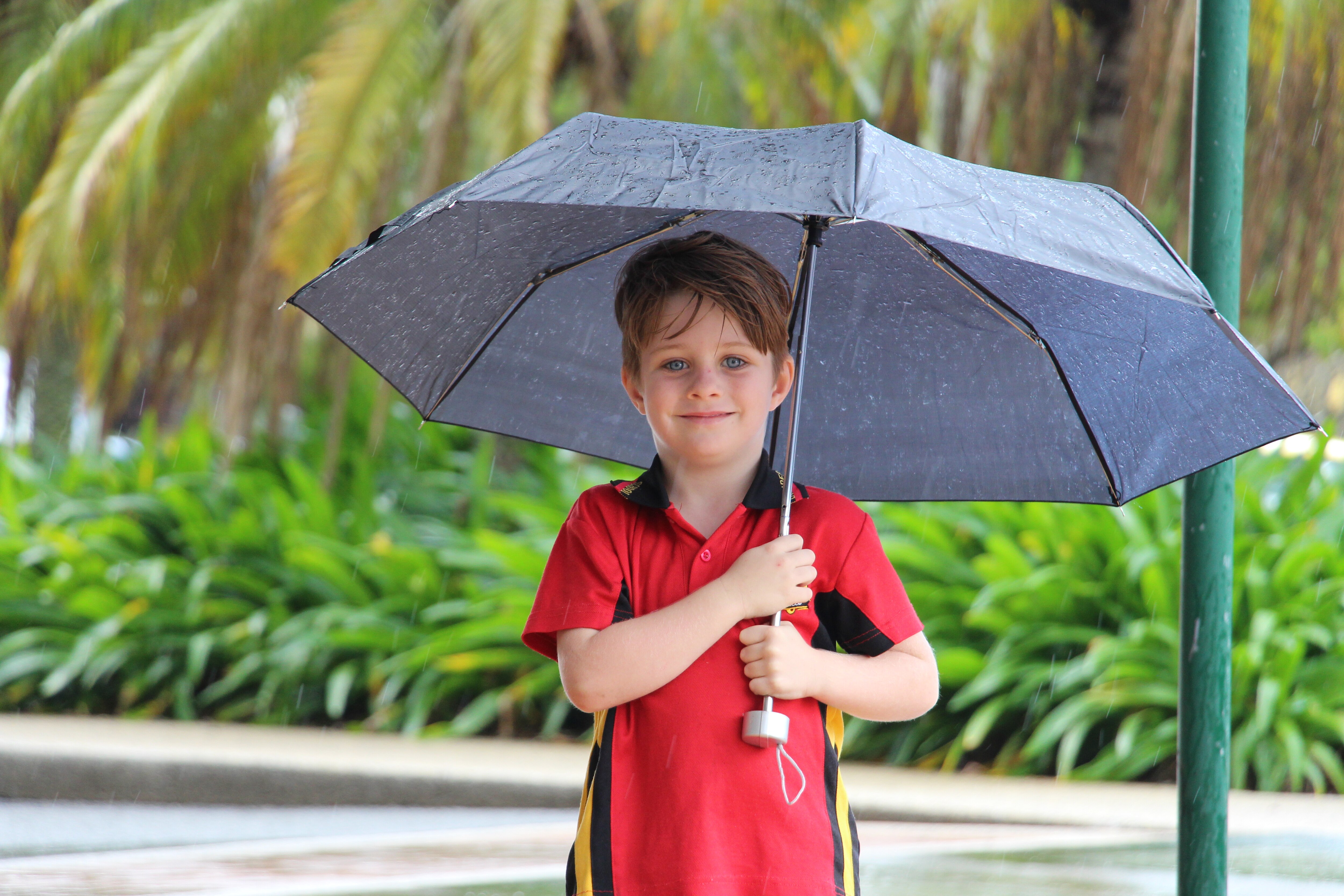 A young boy in a school uniform smiling while holding an umbrella over his head.
