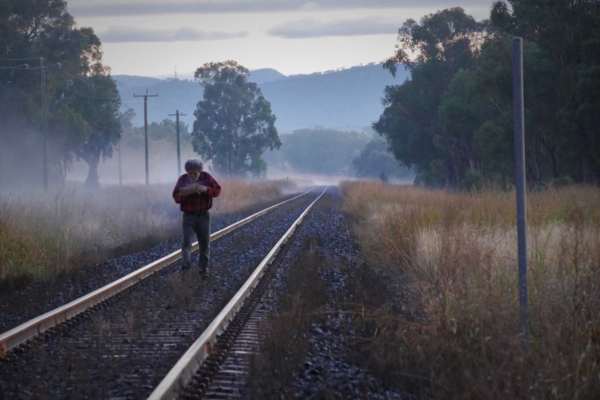 An elder aboriginal man walks down train tracks during a smoking ceremony