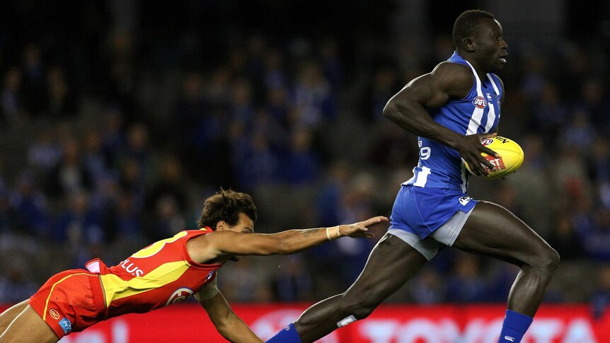 Majak Daw outruns a diving Callum Ah Chee during the round 16 AFL match between the Kangaroos and Suns.