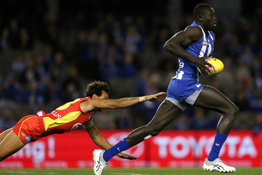 Majak Daw outruns a diving Callum Ah Chee during the round 16 AFL match between the Kangaroos and Suns.