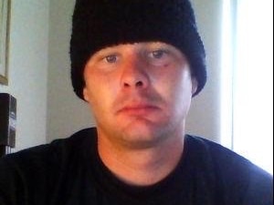 Christopher looks into the camera. He wears a black woolen beanie and black t-shirt.