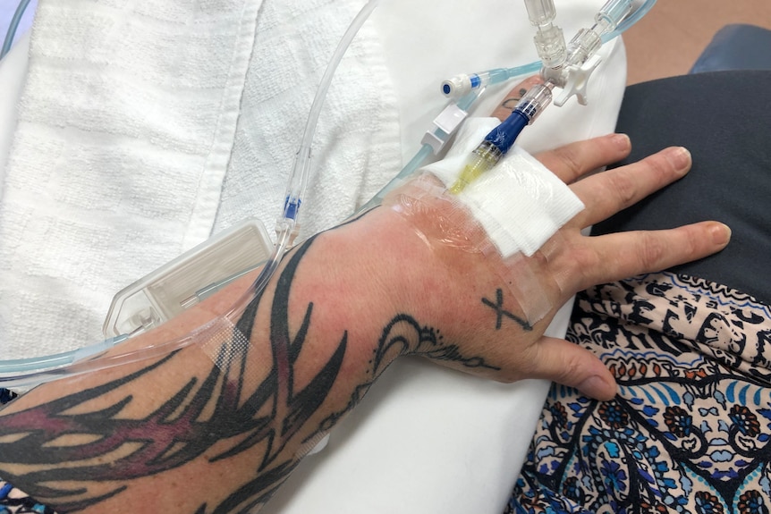 a close up of a woman's tattooed arm with an IV drip entered in the hand