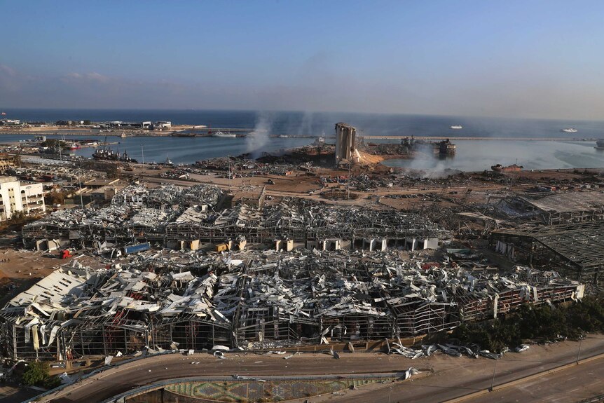 Smoke rises and buildings lie in ruins along a coast line.