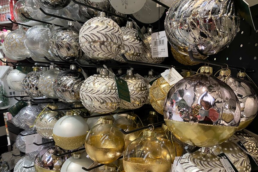 Silver and gold Christmas tree decorations hang in a store for sale.