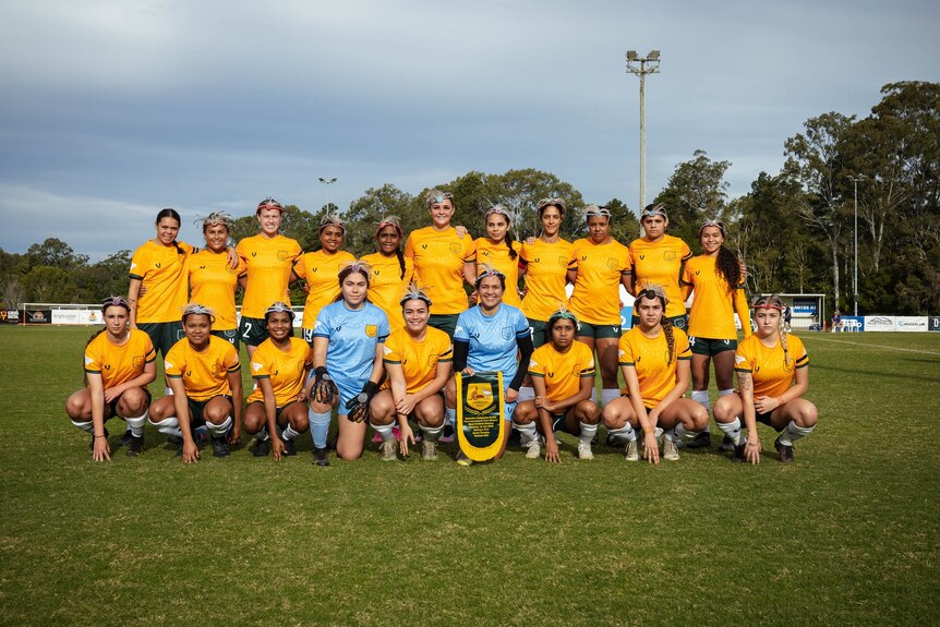The Australian Indigenous Koalas women's soccer team stands together, dressed in their green and gold uniforms