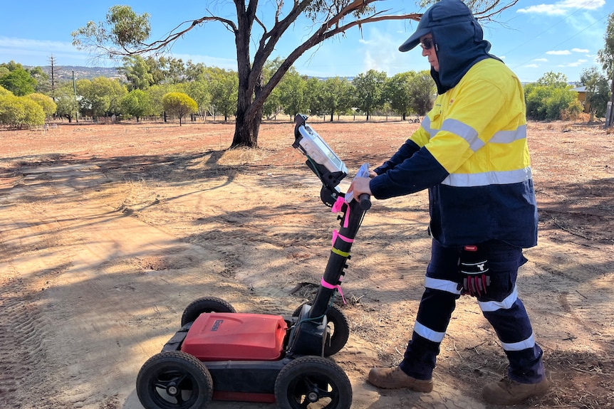 A man pushes a device along dirt ground to map what's underneath a cemetery.