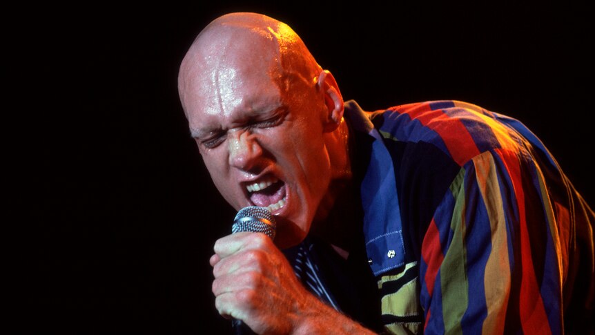  Peter Garrett sweating on stage screaming into a microphone leaning foward in bright, stripped shirt 