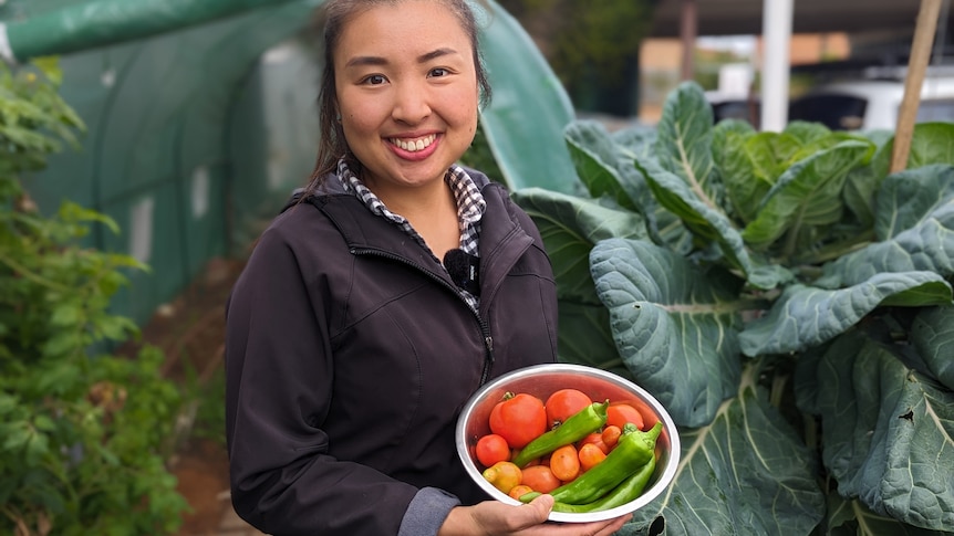 Demi Tsai, a young Taiwanese woman, smiling and holding a bowl of fresh picked capsicums, chillies and tomatoes. 