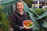 Demi Tsai, a young Taiwanese woman, smiling and holding a bowl of fresh picked capsicums, chillies and tomatoes. 