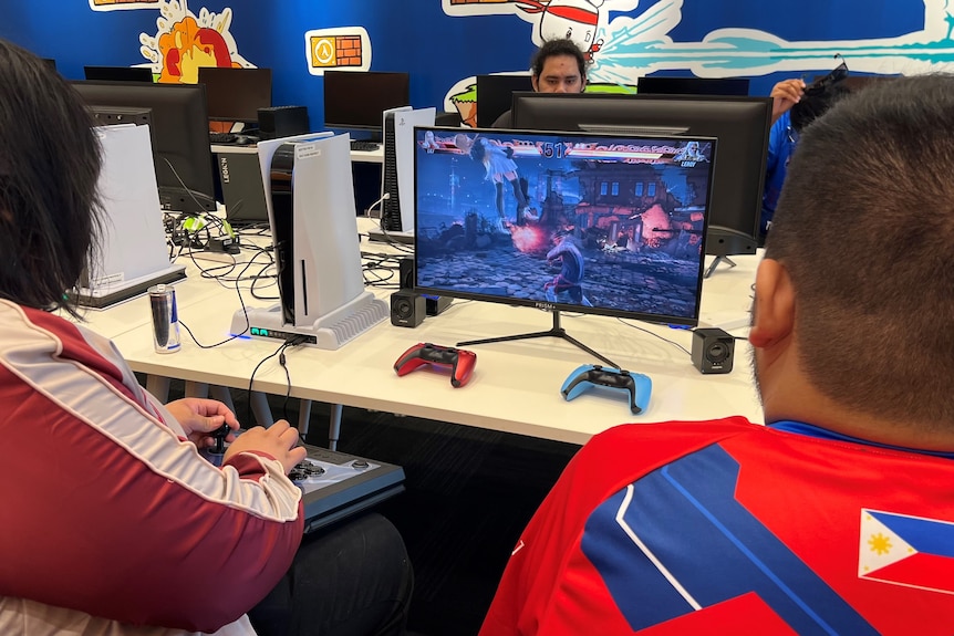 Два человека играют в видеоигру, глядя на экран монитора.