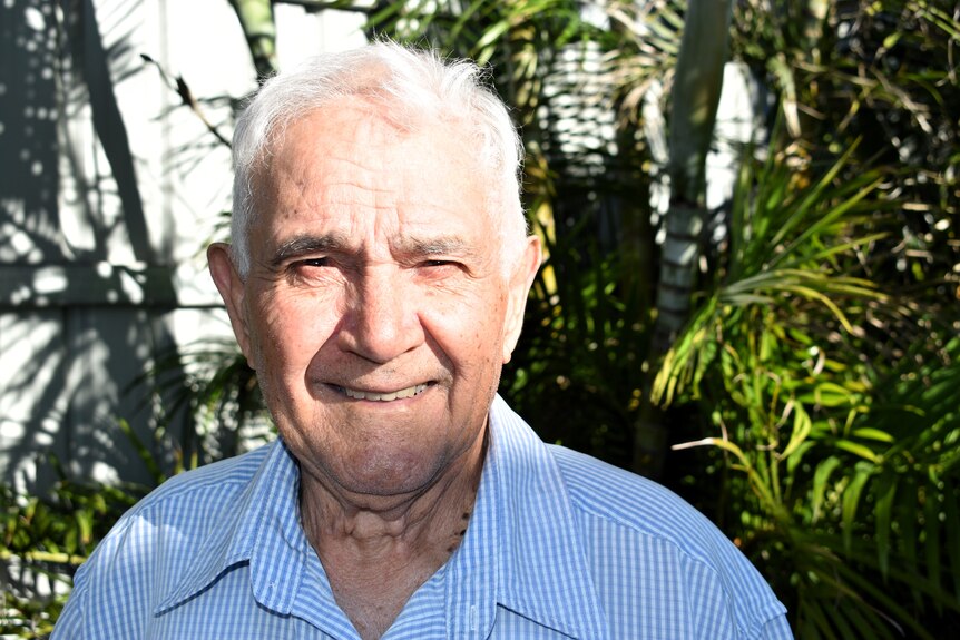 A man in his eighties smiles into camera, with a ray of sunlight across his face.