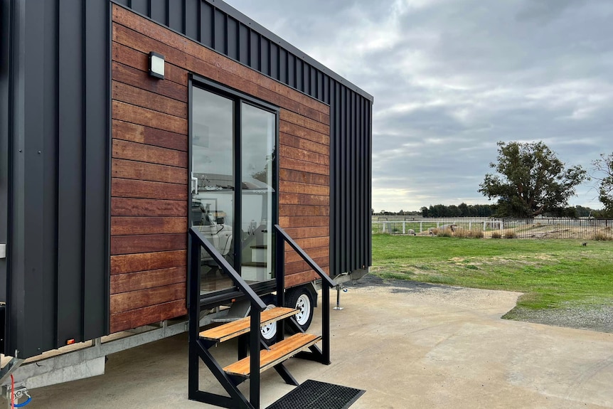 A black tiny home on wheels in a paddock 